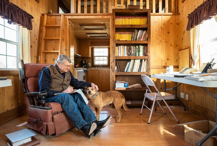 John R. Erickson sitting in a chair writing in his cabin while petting his dog Rosie. 